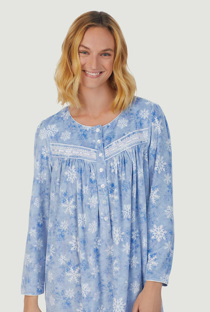 A lady wearing blue long sleeve cozy  fleece gown with snowflake wonderland print.