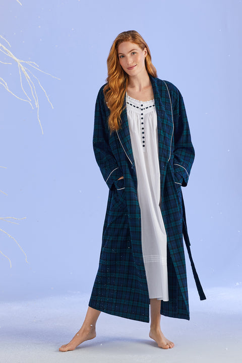 A lady wearing a white long sleeve cotton and blackwatch tartan nightgown.